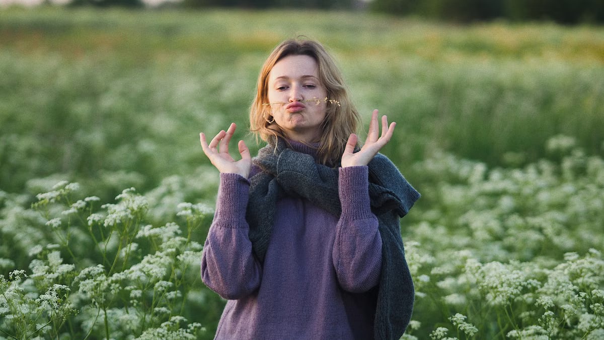 Young woman playfully pouts in a lush, blooming meadow during spring.